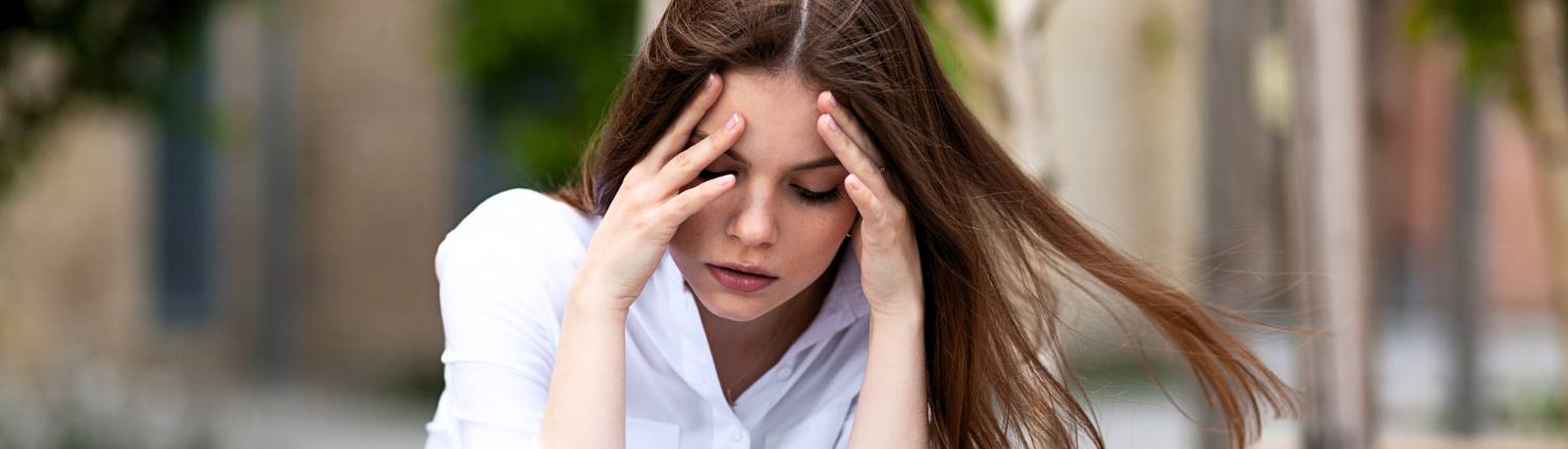 White distressed female with a white blouse sitting in a park with her hands on forehead. Needs help from a therapist specializing in trauma therapy columbus ohio.